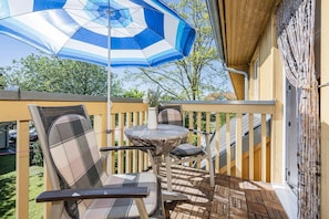 Eine überdachte Terrasse im Freien mit Tisch und Stühlen, einem blau-weiß gestreiften Sonnenschirm und einem Holzzaun.