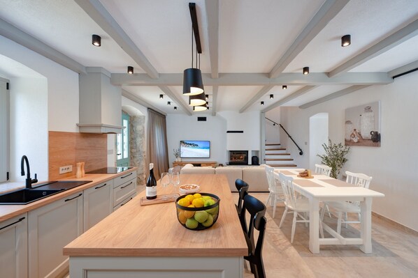 A modern kitchen with a wooden island, white cabinetry, and a dining area with white chairs and a table.