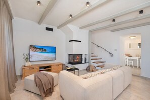 A modern living room with a fireplace, a television, and a staircase leading to an adjacent room.