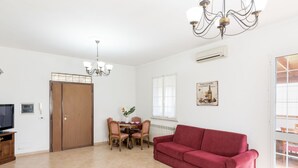 En rummelig opholdsstue med en rød sofa, et spisebord med stole, en lysekrone og et stort vindue.