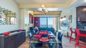 A modern dining area with a glass table set for four, surrounded by dark furniture. A large window offers a view of the outdoors. - Las Palomas 1 BR 1BA Cortez 605 (Puerto Peñasco)