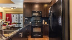A modern kitchen with dark cabinetry, a black refrigerator, a microwave, and a stove. - Las Palomas 1 BR 1BA Cortez 605 (Puerto Peñasco)