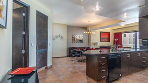 A modern kitchen with dark cabinetry, a central island, and a dining area with red chairs. - Las Palomas 1 BR 1BA Cortez 605 (Puerto Peñasco)