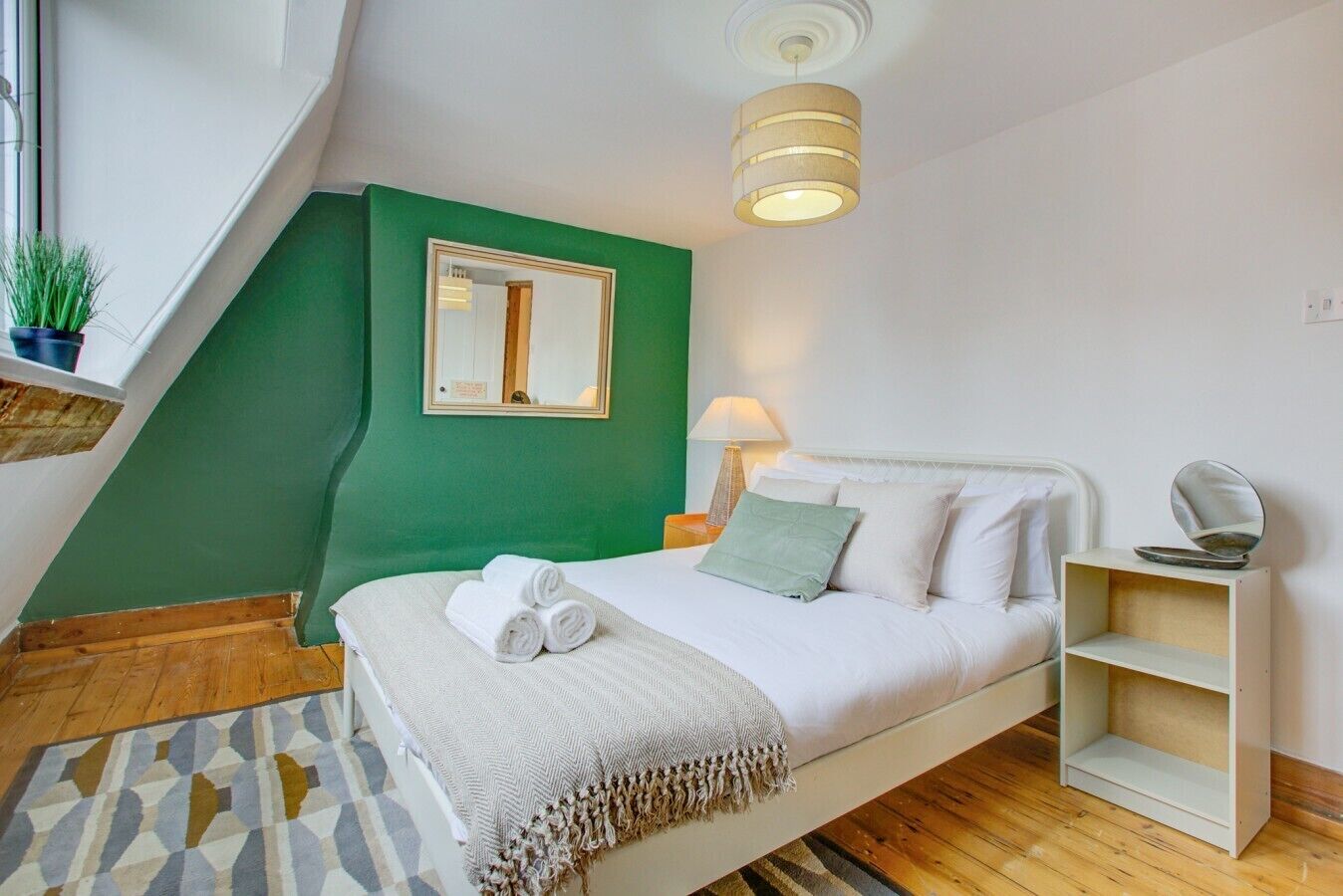 Una camera da letto con un letto, un comodino, una lampada, uno specchio, uno scaffale e una parete verde decorativa.