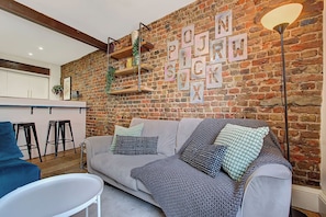 A cozy living area with a brick wall, a sofa with patterned cushions, a coffee table, and a hanging light fixture. - Shoreditch Townhouse, Near Tube | Wi-Fi | Smart TV (London)