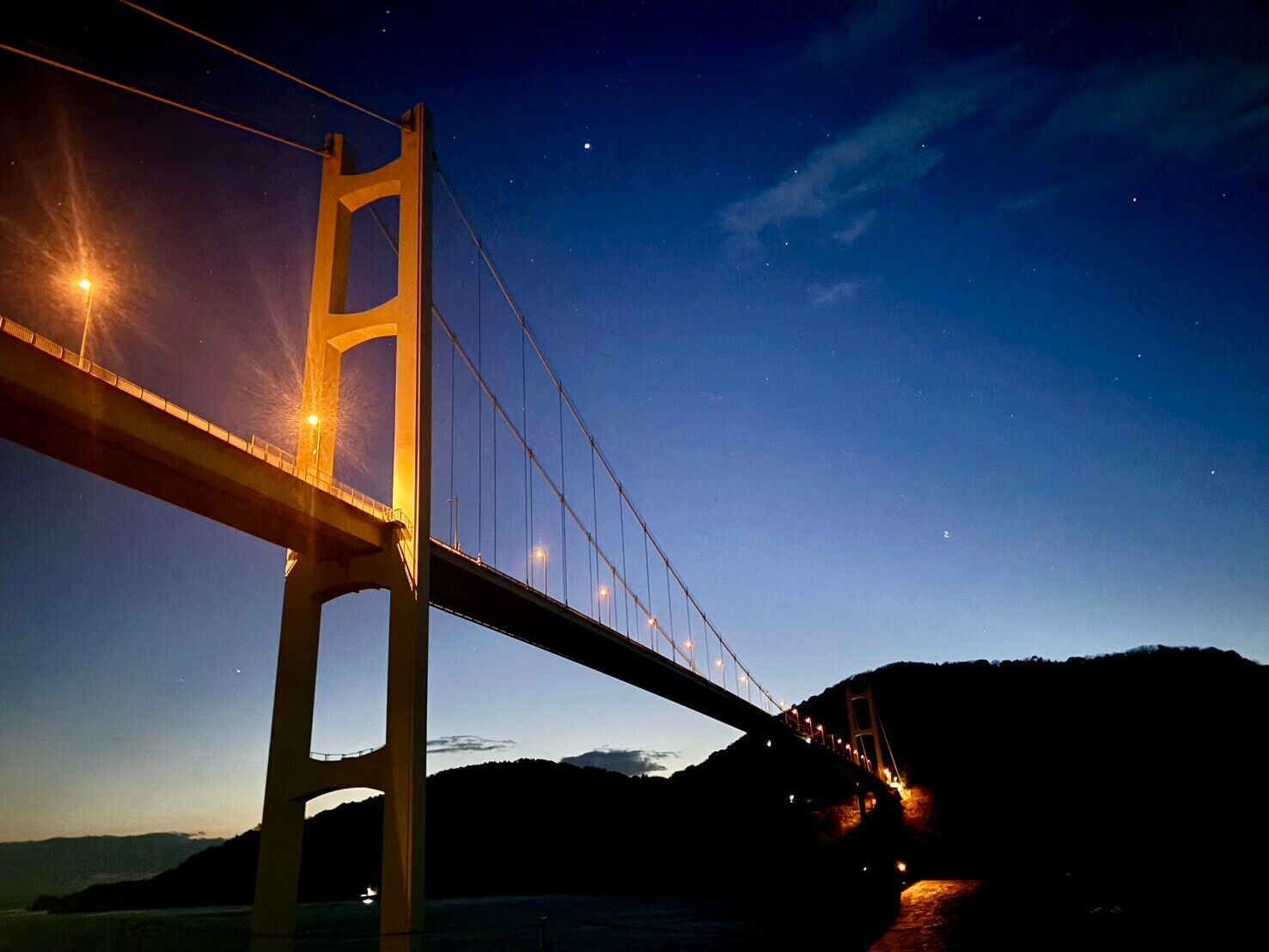 Vista nocturna de un gran puente colgante con cables y torres iluminados.