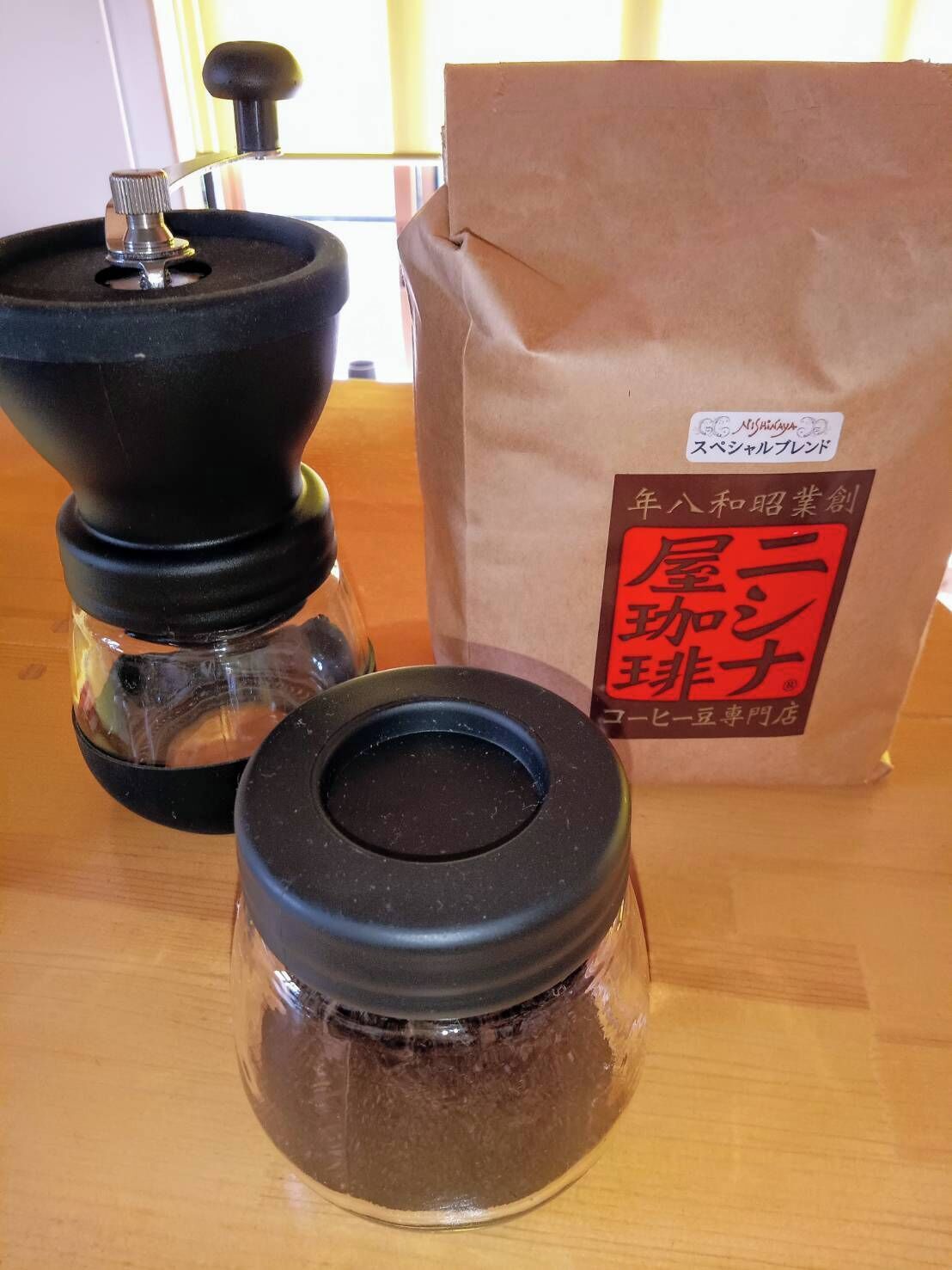 Un moulin à café et un sac en papier avec du texte en japonais, posés sur une table en bois.