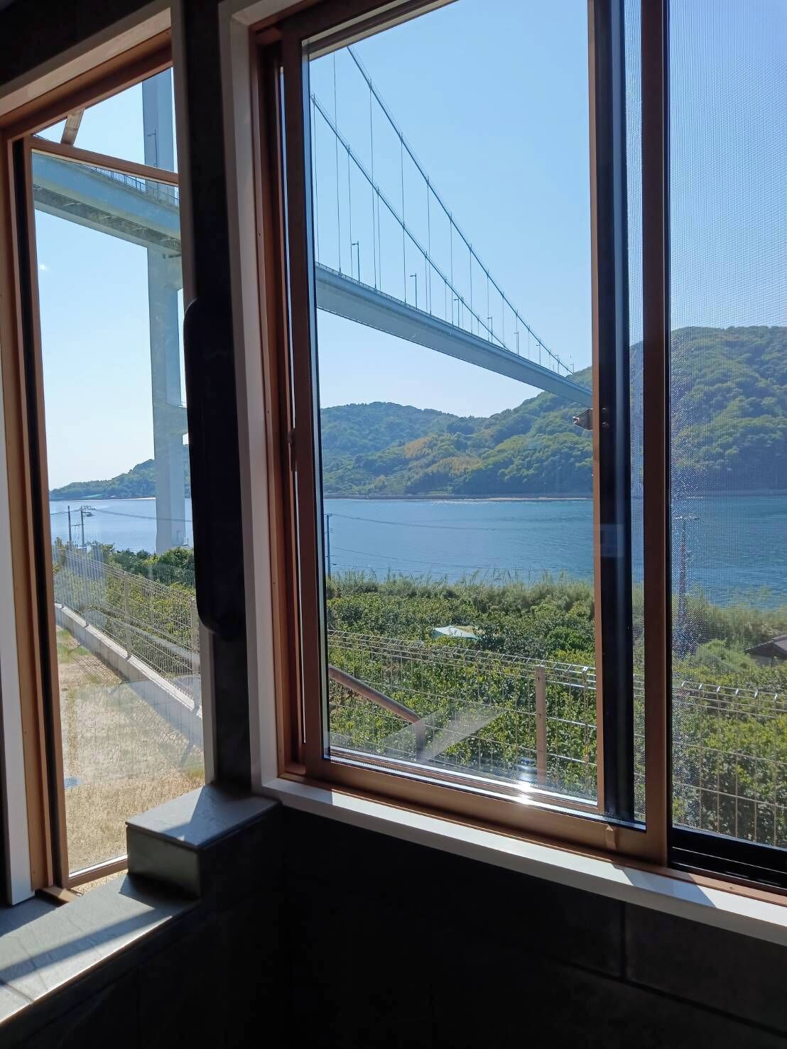 A room with a large window overlooking a bridge, a body of water, and a hilly landscape.