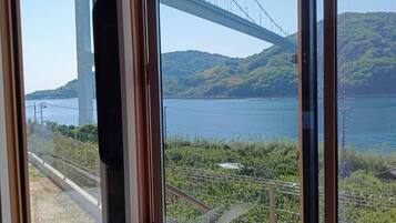 A room with a large window overlooking a bridge, a body of water, and a hilly landscape.