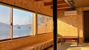 Habitació amb grans finestres que donen a un cos d'aigua, amb seients de fusta, esteves de tatami i un sostre amb bigues al descobert.