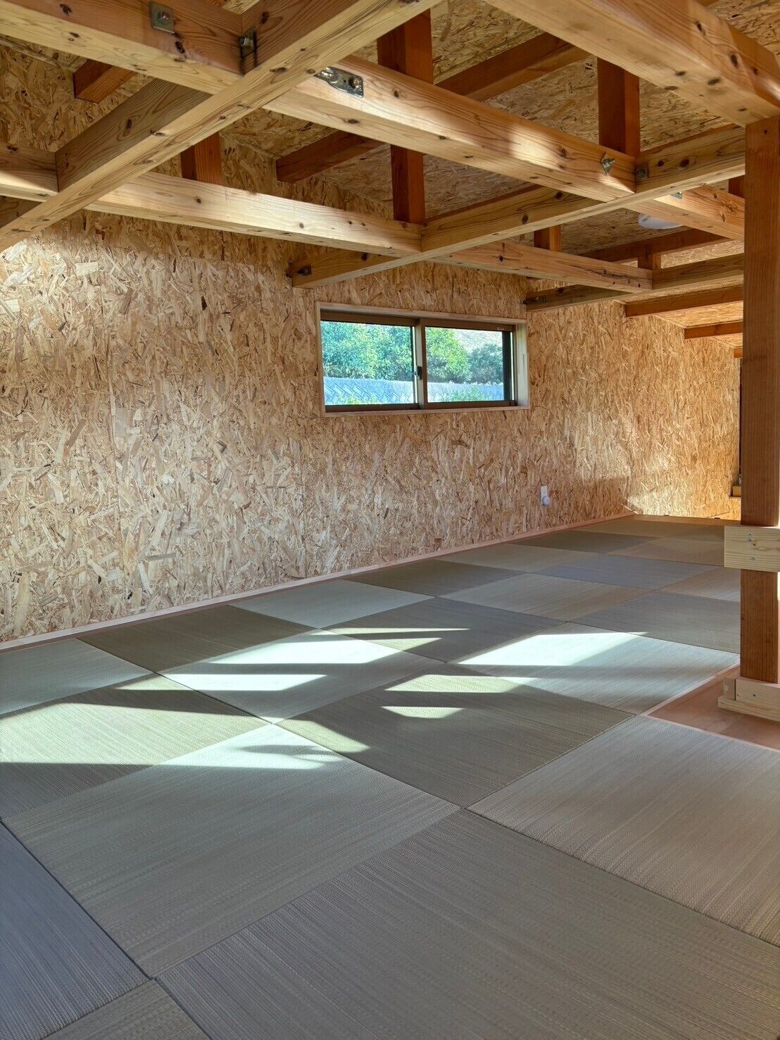 Una habitación con vigas de madera, un ventanal y esteras de tatami.