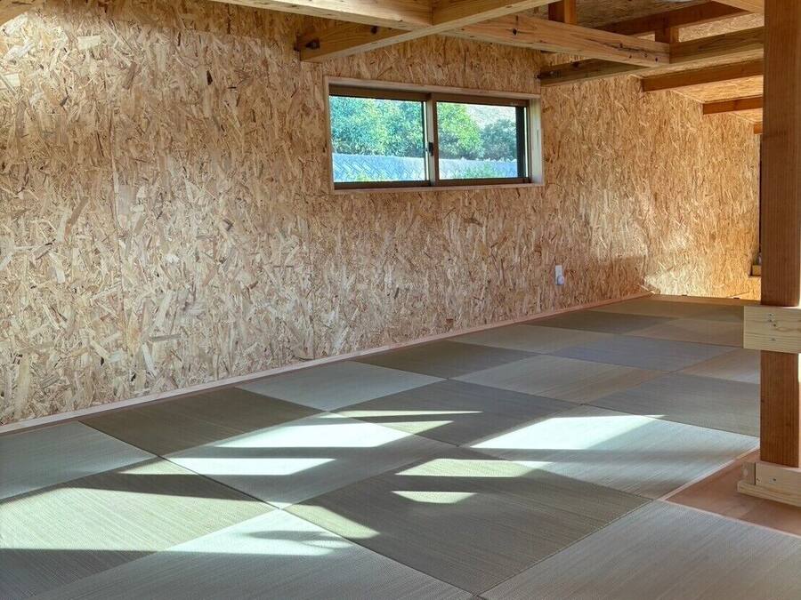 Una habitación con vigas de madera, un ventanal y esteras de tatami.