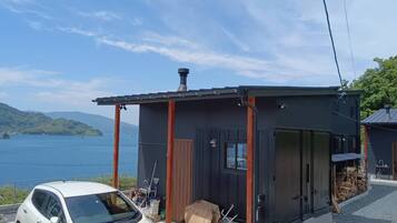 A small cabin with a porch, a car parked in front, and a lake view.