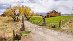 A rural landscape with a wooden house, a dirt road, and a fenced area.