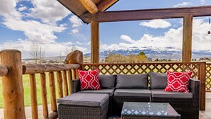 A covered outdoor seating area with wicker furniture and a view of snow-capped mountains.