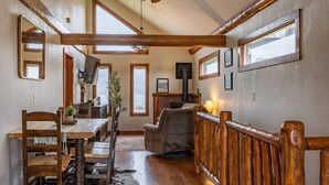 A rustic interior with wooden beams, a dining area, a fireplace, and a view of the outdoors.