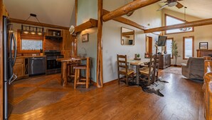 A spacious kitchen with wooden beams, a dining area with a wooden table and chairs, and a large window overlooking a scenic view.