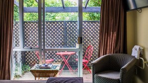 Ein Zimmer mit einem Bett, einem Sessel, einem kleinen Tisch und Blick auf einen Garten durch eine Glastür.