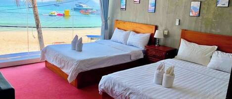 A hotel room with two beds, a red carpet, a view of the beach, and a window with a curtain.