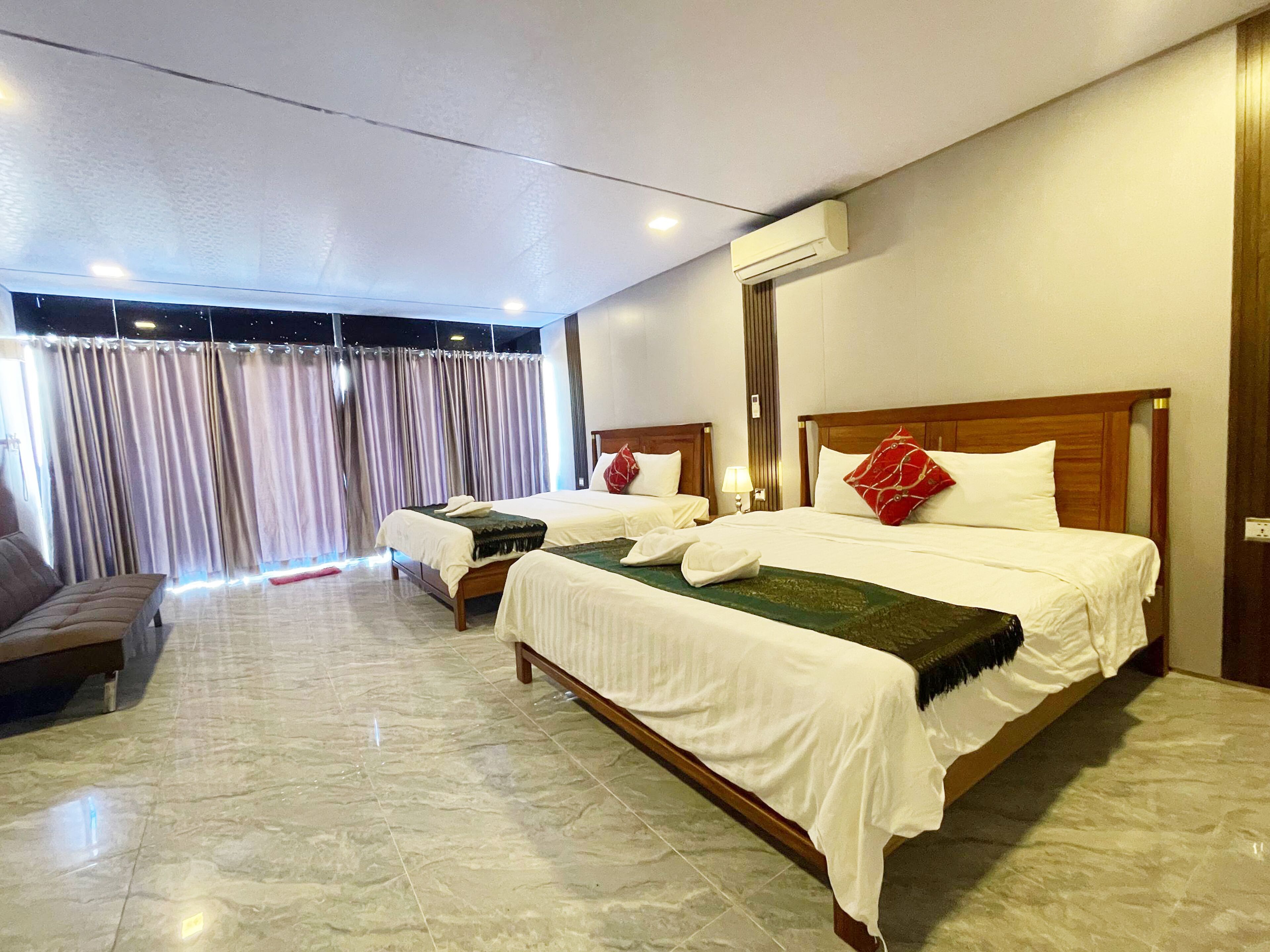 Una habitació d'hotel amb dos llits, un sofà i una finestra gran amb cortines.