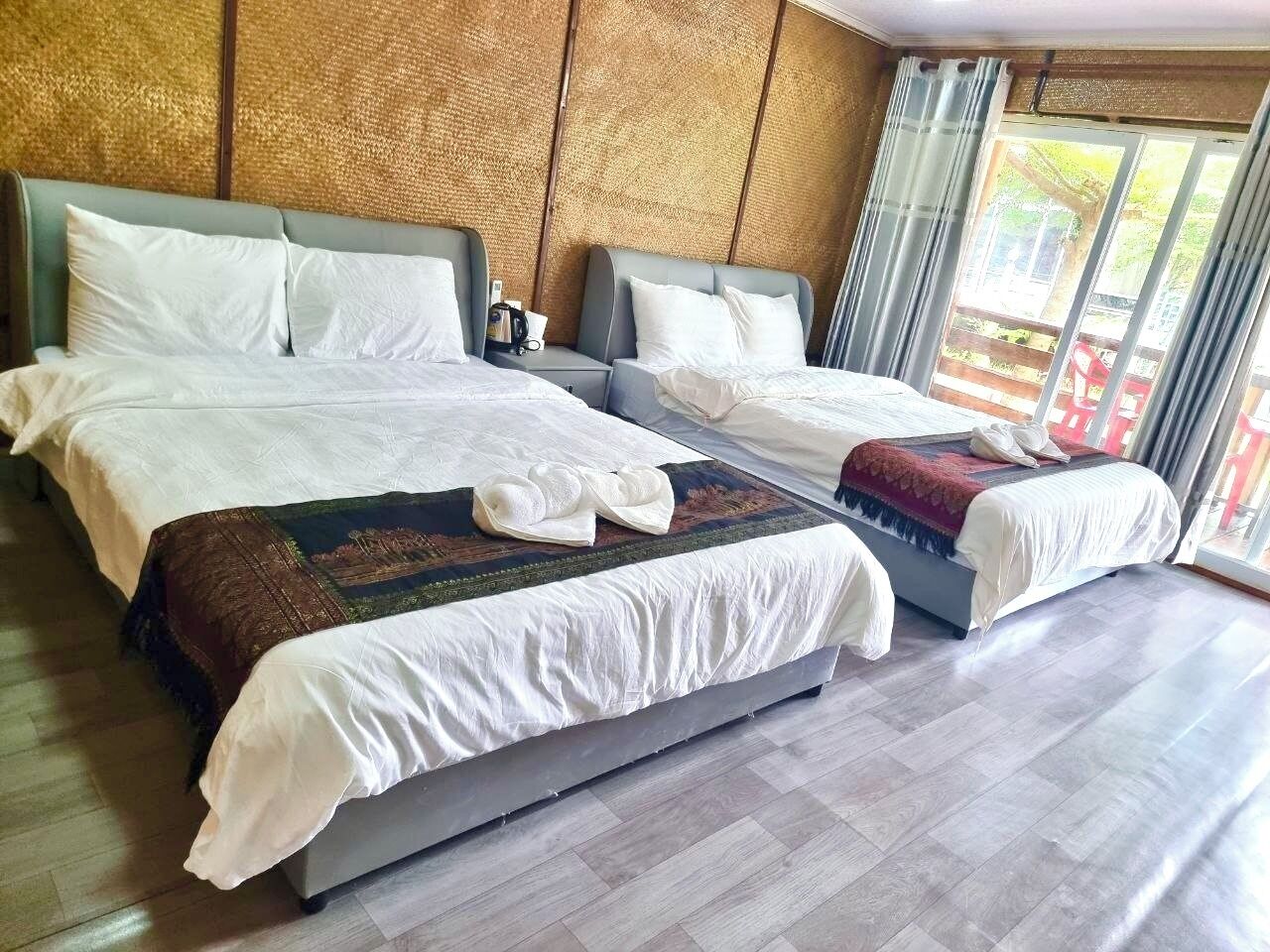 A hotel room with two beds, a large window with curtains, and a wooden textured wall.