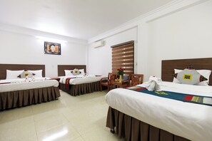 A hotel room with two beds, a small table with a vase, and a wall-mounted air conditioner.