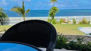 Une vue depuis un balcon donnant sur une clôture blanche en bois, un palmier et un ciel bleu dégagé.