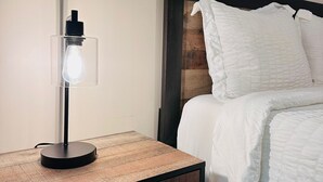 Un lit bien fait, avec une literie blanche, une table de chevet avec une lampe et une tête de lit en bois.