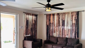 Un salon comprenant un canapé, deux fauteuils, une table basse, un ventilateur de plafond et un tapis à motifs.
