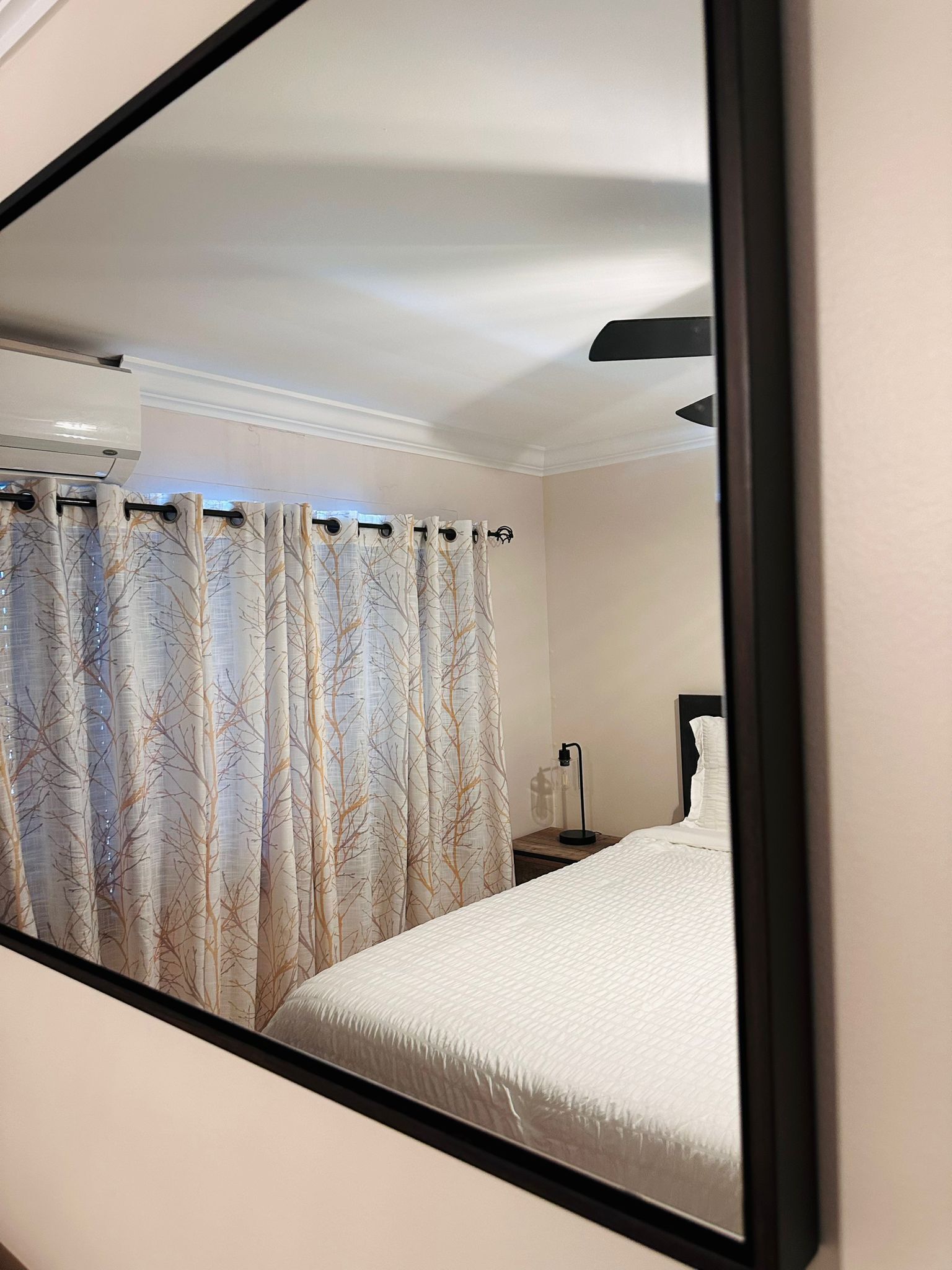 Une chambre à coucher avec un lit, une table de chevet, une lampe et une fenêtre avec des rideaux.