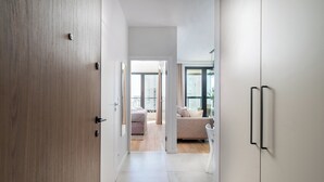 A modern interior with a hallway leading to a living area with a sofa and a window. - Grzybowska Beige City View Apartment (Warszawa)