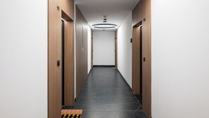 A modern hallway with wooden doors, a black tiled floor, and a circular light fixture on the ceiling. - Grzybowska Beige City View Apartment (Warszawa)