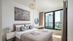 A modern bedroom with a large bed, a bedside table, a nightstand, a mirror, and a city view through a large window. - Grzybowska Beige City View Apartment (Warszawa)
