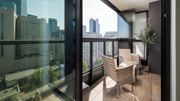 A balcony with wicker furniture, a potted plant, and a city view. - Grzybowska Beige City View Apartment (Warszawa)