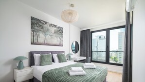 Een moderne hotelkamer met een groot bed, uitzicht op de stad, een schilderij aan de muur en een bureau met een lamp.