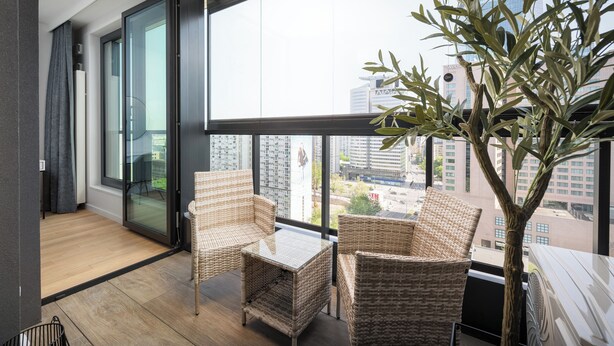 Een balkon met rieten meubilair, een glazen deur en uitzicht op stadsgebouwen.