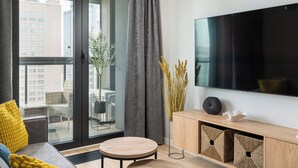 Een moderne woonkamer met een grote televisie, een bank, een ronde tafel en een balkon met uitzicht op gebouwen.