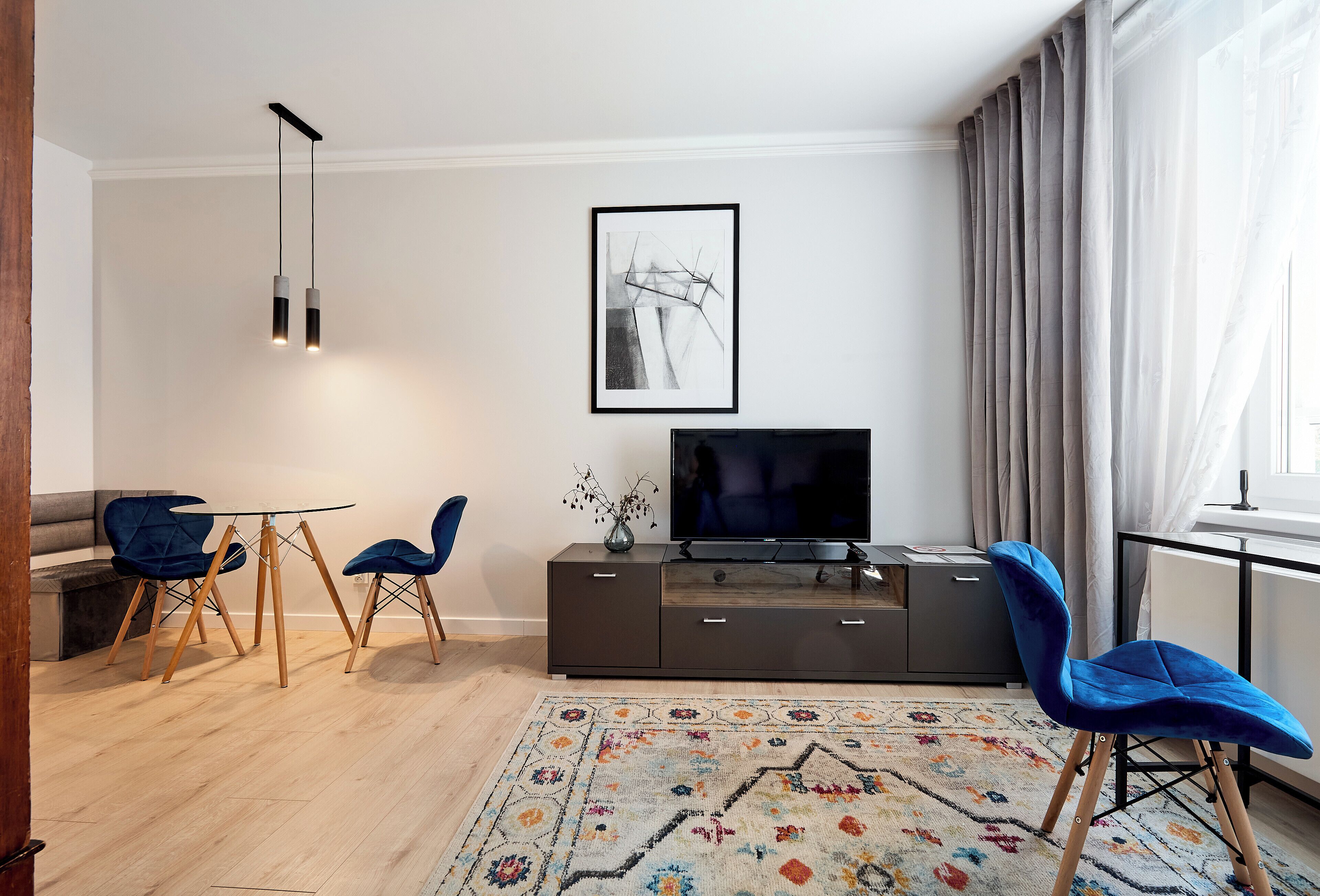Ein modernes Wohnzimmer mit einer Couch, zwei blauen Sesseln, einem Fernseher und einem gemusterten Teppich.