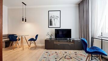 Ein modernes Wohnzimmer mit einer Couch, zwei blauen Sesseln, einem Fernseher und einem gemusterten Teppich.
