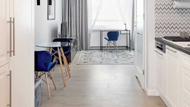 Een moderne keuken met witte kasten, een eethoek met een blauwe stoel, en een groot raam met transparante gordijnen.