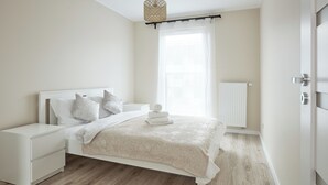 Une chambre à coucher avec un lit, des tables de chevet, un radiateur et une fenêtre avec des rideaux.