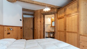 Une chambre à coucher en bois, avec un lit, une armoire en bois et une salle de bain visible à travers une porte ouverte.
