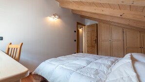 Una camera da letto con soffitto in legno, un letto con biancheria da letto bianca, una sedia di legno e un lampadario a parete.