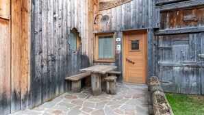 Un edificio rustico in legno con una porta in legno, un patio in pietra e una panchina in legno.