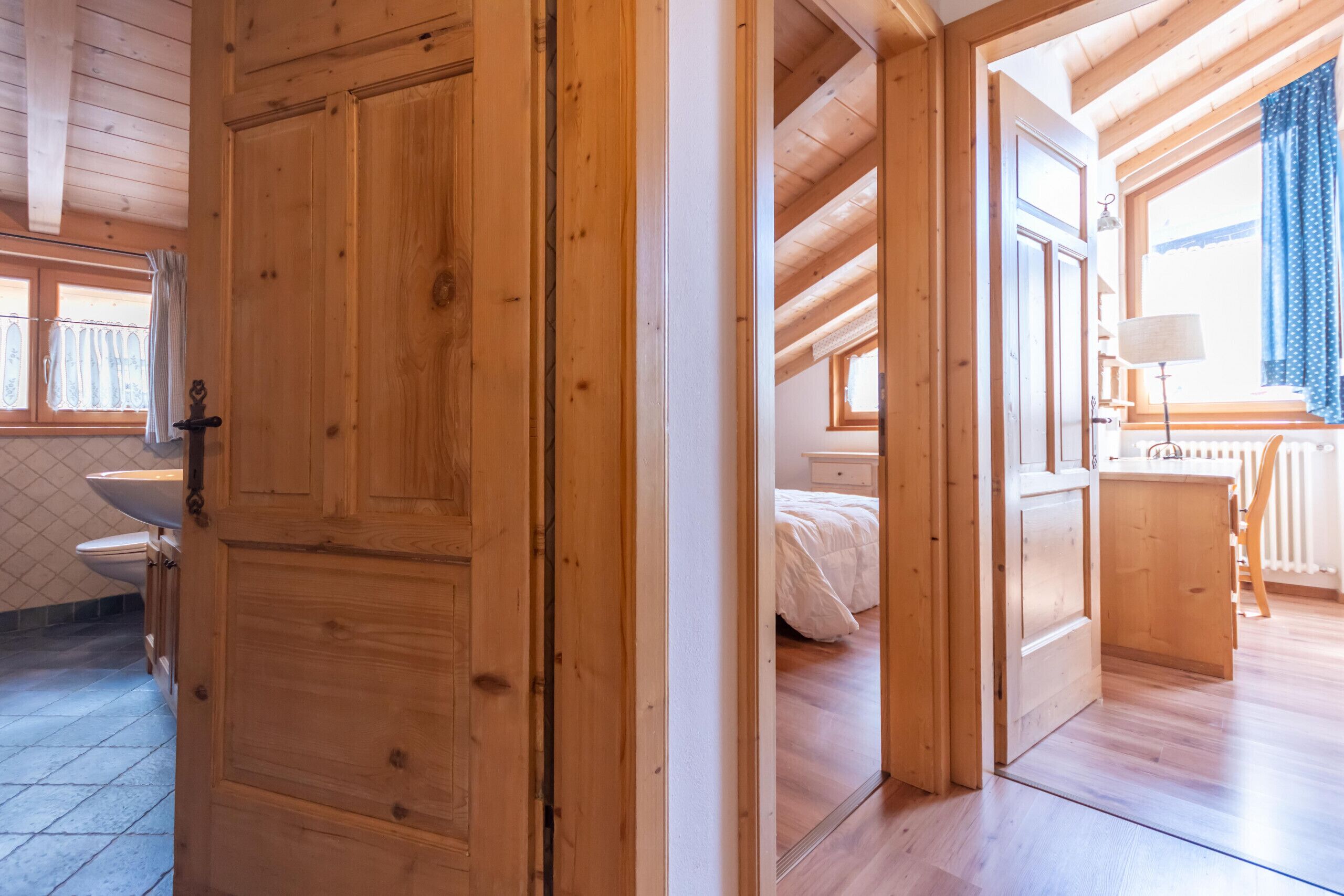 A wooden interior with a large door, a bed, a bedside table, and a window with curtains.