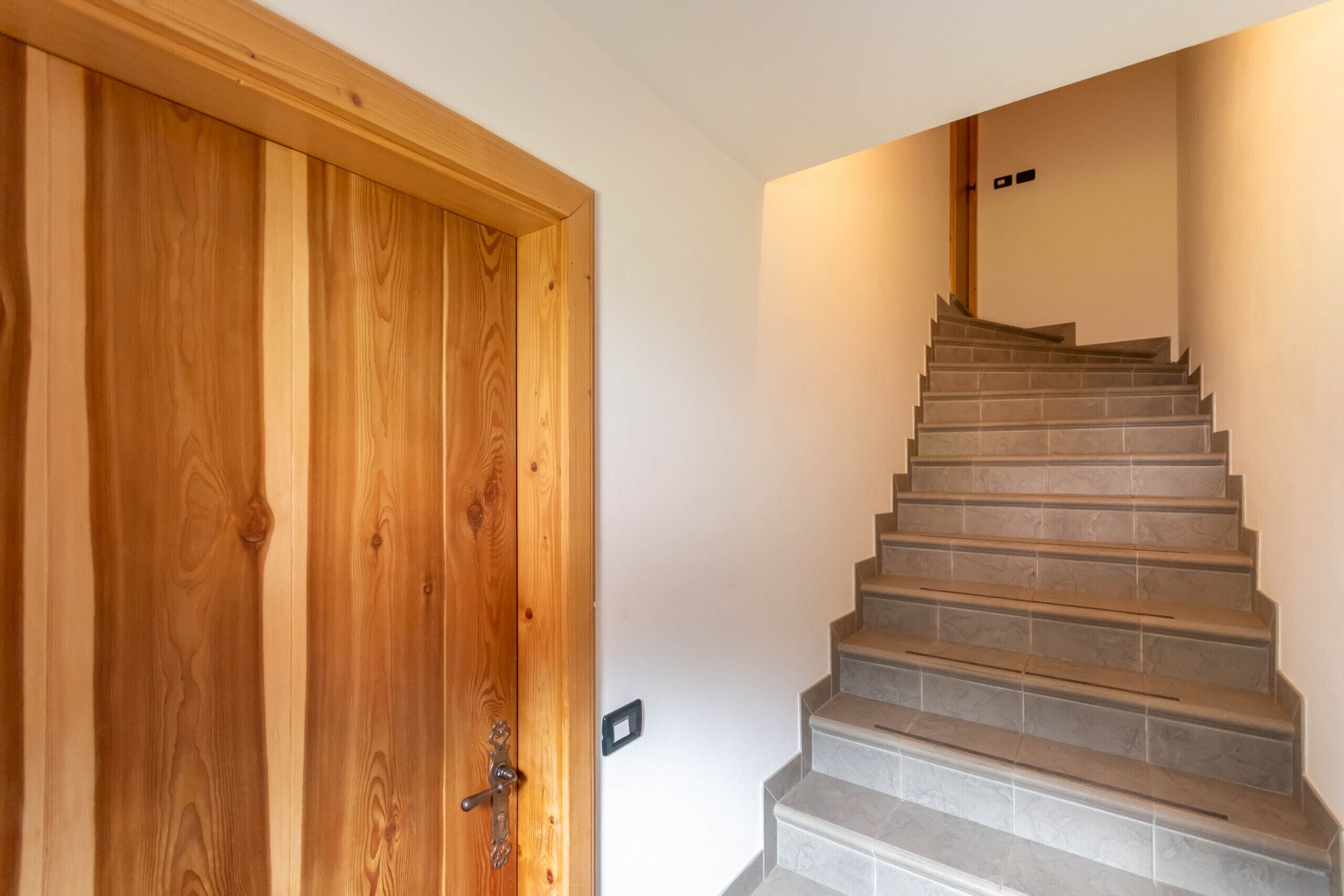 A wooden door with a metal handle and a staircase with grey tiles leading to a landing.