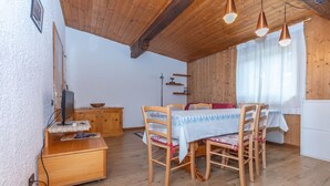 Una habitación acogedora con suelo de madera, una mesa de comedor con sillas, un televisor sobre un mueble de madera y una ventana con cortinas.