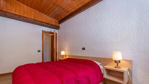 Un dormitorio con techo de madera, colcha roja, dos lámparas de noche y mesita de noche de madera.