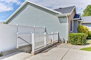 Une maison d’habitation avec une clôture en bois peinte en blanc, une allée en béton et une pelouse bien entretenue.
