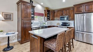 Una cocina moderna con armarios de madera, electrodomésticos de acero inoxidable y una isla central con taburetes de bar.